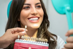 Smiling woman examining her teeth shade with a dental professional using a shade guide, illustrating the Opalescence Boost teeth whitening process.